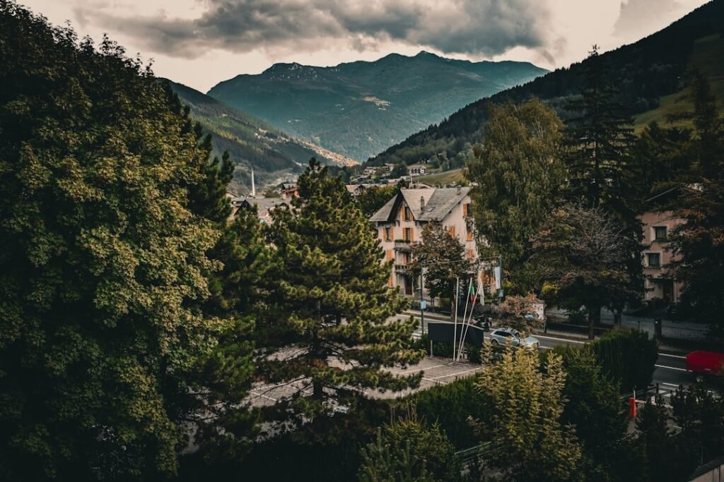 A village nestled between forested mountains under a cloudy sky.